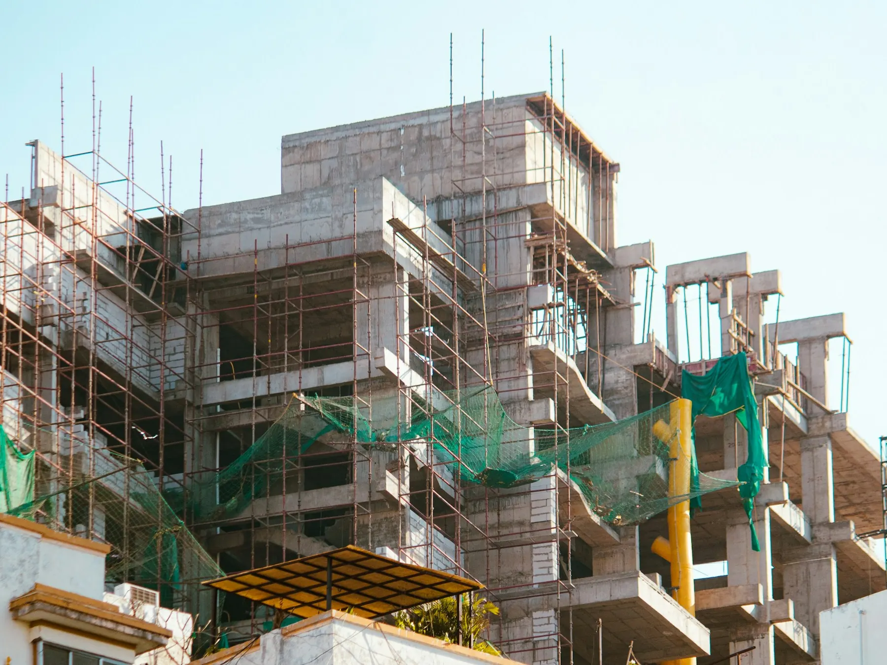 Multi-storey building under construction wrapped in steel scaffolding and green safety netting in Ahmedabad, India